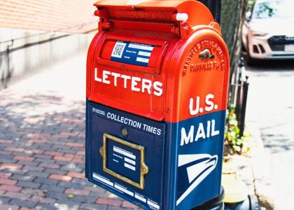 Vibrant U.S. mailbox on a city sidewalk with a parked car, conveying a classic urban scene.