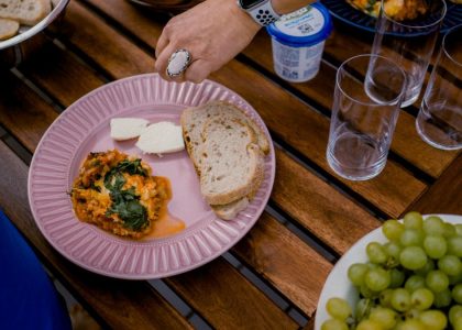 A casual outdoor dining table with bread, greens, and a side dish for brunch.